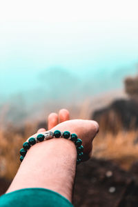 Close-up of cropped hand wearing bracelet against sky