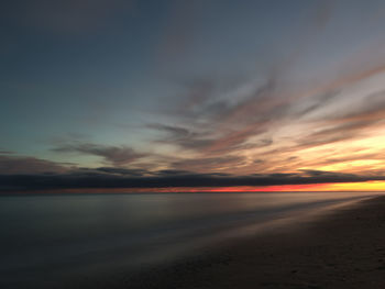 Scenic view of beach against dramatic sky during sunset