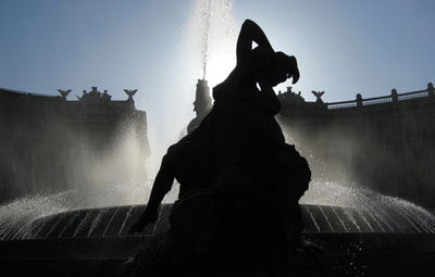 Silhouette statue by fountain against clear sky