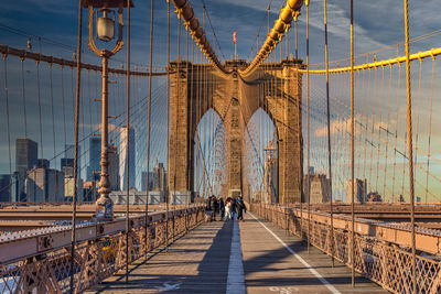 Brooklyn bridge daylight view with people walking, the american flag at its top and skylines 