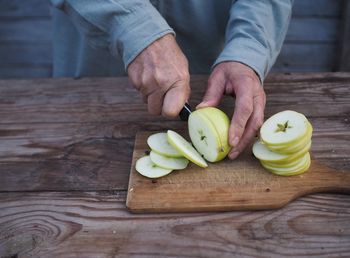 Closeup adult woman hands cutting fresh green apples on wooden cutting board 