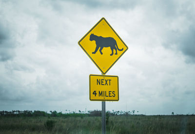 Road sign on field against sky