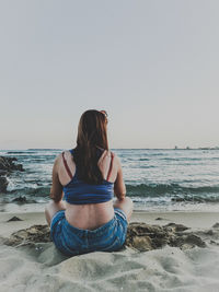 Rear view of woman sitting on beach against clear sky