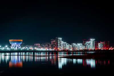 Illuminated buildings by river against sky at night