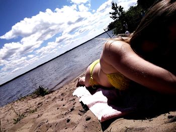 Woman relaxing on beach against sky