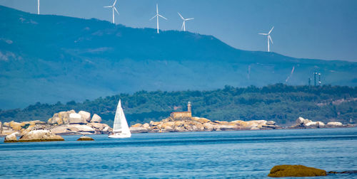 Sailboat on sea by mountain against sky