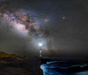 Illuminated lighthouse at beach against star field at night