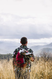 Rear view of traveler with dog in backpack on top of mountain person