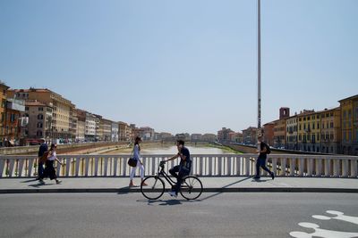 People riding bicycle on road in city against clear sky