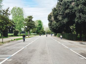 People on road amidst trees in city against sky
