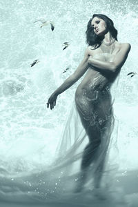Digital composite image of naked woman covering breast with plastic while standing against sea