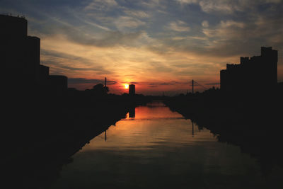 Silhouette bridge over river against sky during sunset