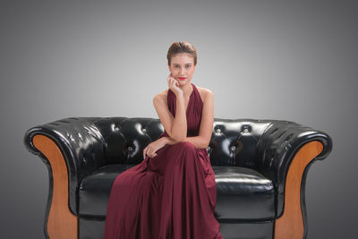 Portrait of young woman sitting against gray background