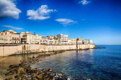 Buildings by sea against blue sky