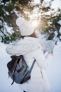 Beautiful young woman at sunset in snowy mountain reading a map. travel, nature and technology