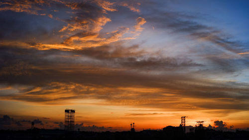 Silhouette buildings against dramatic sky during sunset