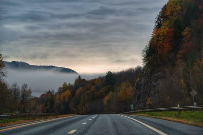 Country road by trees against sky