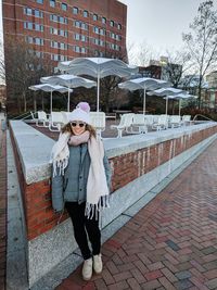 Portrait of young woman by retaining wall against sidewalk cafe