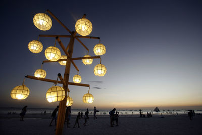 Illuminated lamp post at beach against sky at dusk