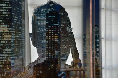 Illuminated buildings seen through window with reflection of man