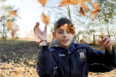 The boy, playing in the park, throws yellow autumn leaves at the camera 