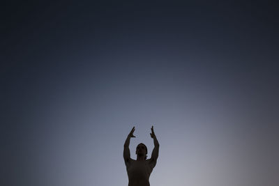 Low angle view of shirtless man standing with arms raised while meditating against sky at night