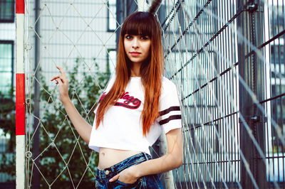 Portrait of young woman standing by chainlink fence