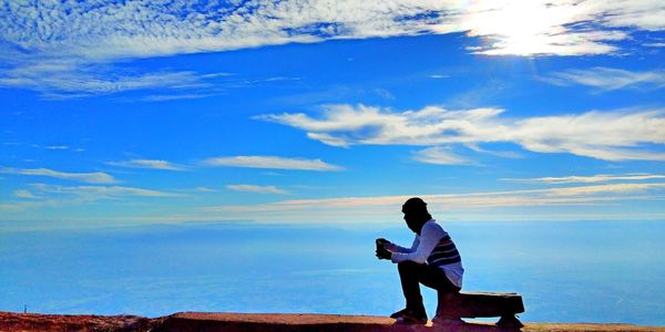 Silhouette man standing against sea against blue sky