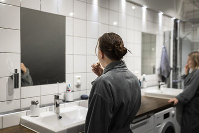 Rear view of young woman brushing teeth in bathroom