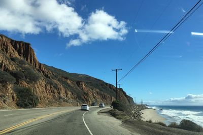 Cars on road by sea against sky