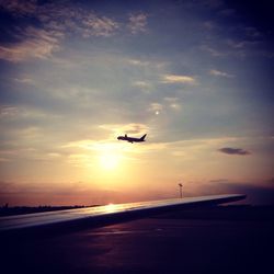 Cropped image of airplane at runway against sky during sunset