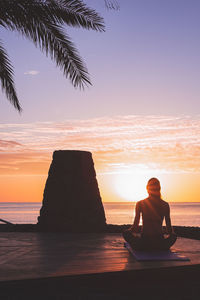 Young woman's silhouette meditating at sunrise in front of the beach. vertical format.