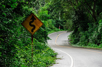 Old traffic sign placed beside along the messy road from tree and grass.