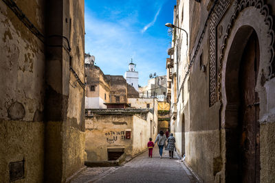 Rear view of people walking on street amidst buildings in city