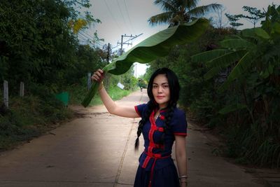 Portrait of young woman holding leaf over head while standing on road