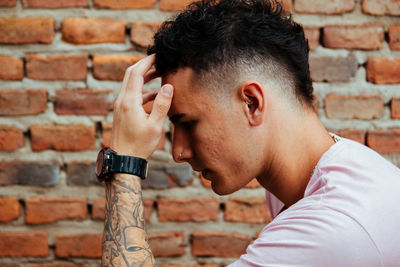 Side view of thoughtful young man against brick wall