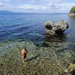 Man standing on rock in sea against sky