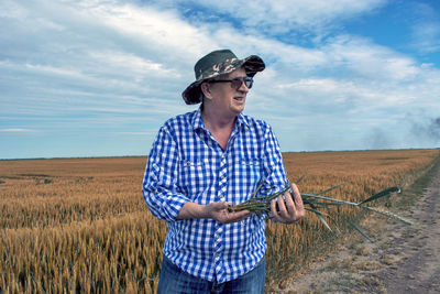 Senior man holding plant standing on field against sky