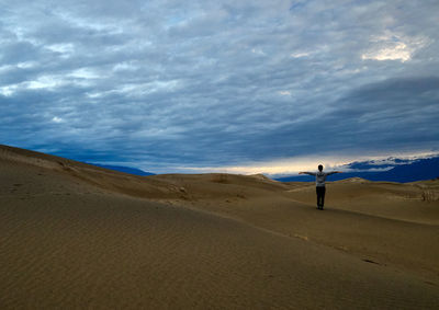 Man standing on sand dune at beach against sky