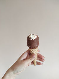 Cropped hand holding ice cream cone against white background