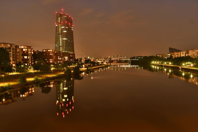 Illuminated buildings by river against sky at night