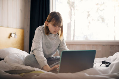 Teenage girl using laptop while doing homework in bedroom