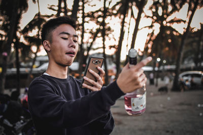 Young man photographing alcohol bottle outdoors