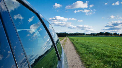 Road passing through grassy field against cloudy sky