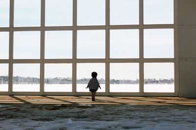 Rear view of child standing on footpath against sky during winter