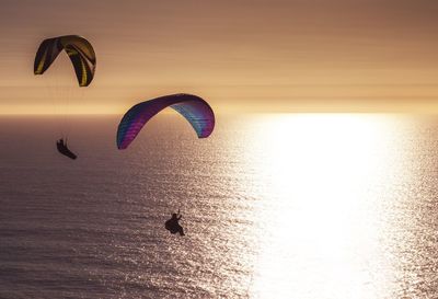 People paragliding over sea against sky during sunset