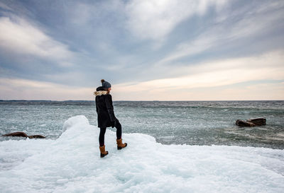 Woman standing on icy shoreline of a lake looking into the distance.