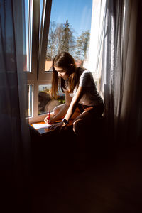 Creative child immersed in drawing sitting by window at home drawing hobby for developing imaginatio