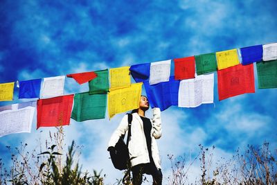 Low angle view of young woman standing by flags against sky