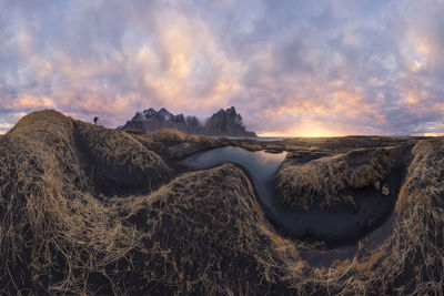 Distant traveler standing on top of mountain range against cloudy sky during sunset near black sand beach in iceland